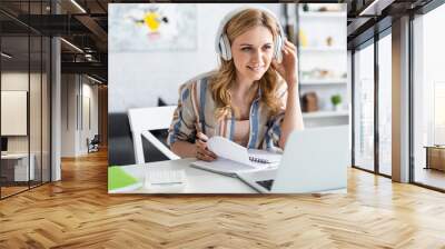 Selective focus of attractive woman in headphones looking at laptop while studying online Wall mural