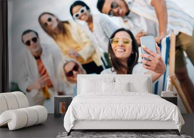 selective focus of attractive young woman taking selfie with multicultural friends having fun on beach Wall mural