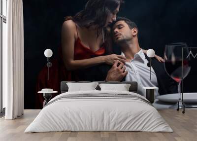 Selective focus of beautiful woman unbuttoning shirt of boyfriend during romantic dinner isolated on black Wall mural