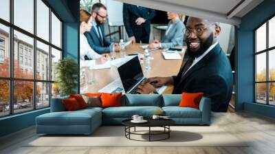 selective focus of cheerful african american man using laptop with blank screen near coworkers Wall mural