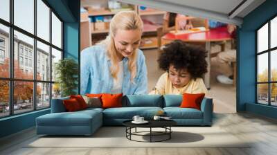 Selective focus of child playing game by smiling teacher with kids at background in montessori school Wall mural