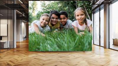 selective focus of cute multicultural children smiling while lying on grass Wall mural