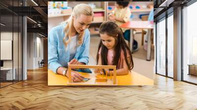 Selective focus of kid and teacher playing wooden game with children at background in montessori school Wall mural