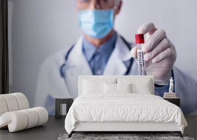 selective focus of mature doctor in medical mask holding test tube with coronavirus blood sample lettering isolated on grey Wall mural