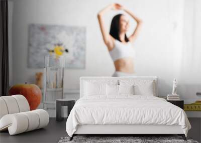 Selective focus of measuring tape, fruits with scales and glass of water on table and sportswoman in kitchen, calorie counting diet Wall mural