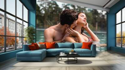 selective focus of muscular man kissing neck of sexy woman in swimming pool Wall mural