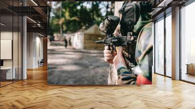 selective focus of paintball player in goggle mask and camouflage aiming by paintball gun outdoors Wall mural