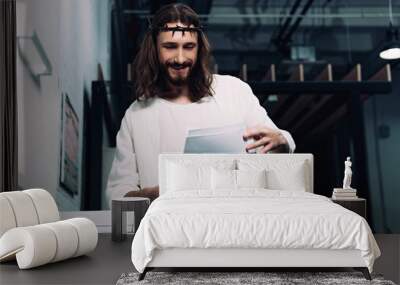 selective focus of smiling Jesus in crown of thorns and robe checking papers near copy machine in modern office Wall mural