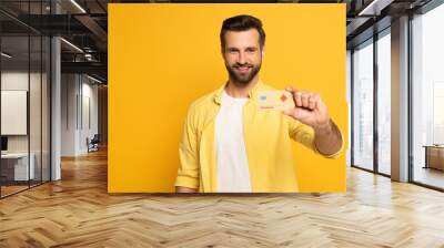 Selective focus of smiling man holding model of credit card isolated on yellow Wall mural