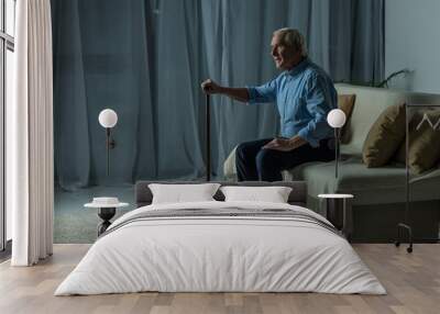 Senior man leans on a cane while sitting on sofa Wall mural