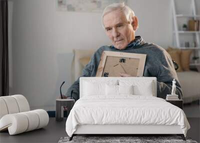 Senior thoughtful man sitting in chair and holding old photo frame Wall mural