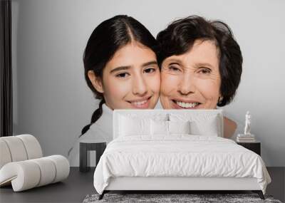 Senior woman smiling near hispanic granddaughter isolated on grey, two generations of women Wall mural