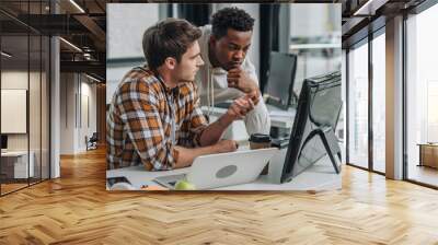 serious programmer gesturing while looking at computer monitor together with african american colleague Wall mural