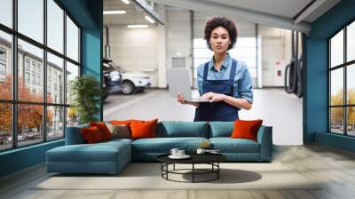 serious young african american mechanic standing with laptop and looking at camera in garage Wall mural