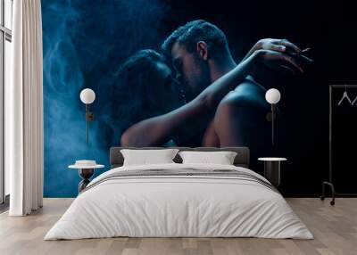 Sexy man kissing girlfriend in bra on black background with smoke Wall mural