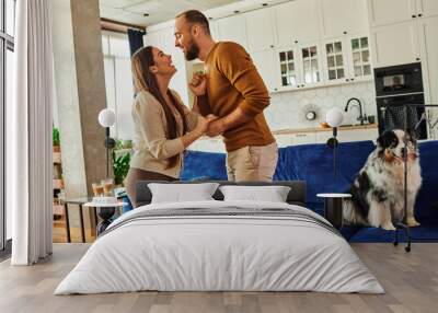 Side view of cheerful couple holding hands and dancing near border collie dog on couch at home Wall mural