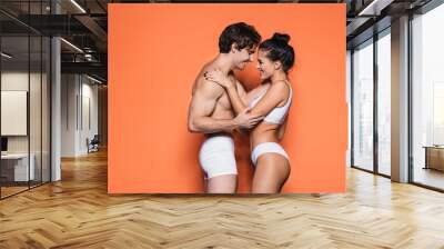 side view of happy and sexy couple in white underwear standing on orange. Wall mural