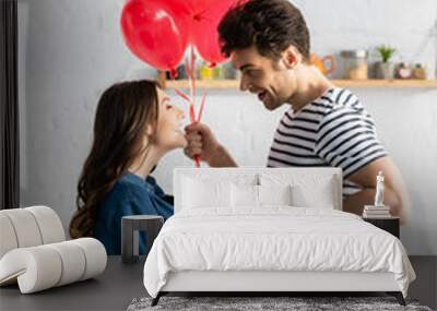 side view of happy man holding heart-shaped balloons and gift box near smiling girlfriend Wall mural