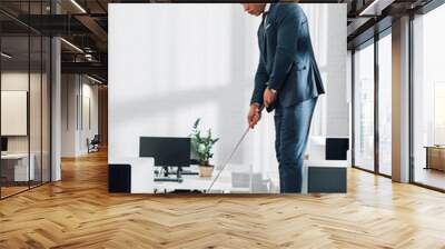 side view of young african american businessman playing golf in office Wall mural