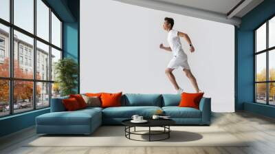 side view of young asian male athlete running on grey background Wall mural