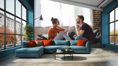 side view of young couple sitting on sofa and talking while looking at each other Wall mural