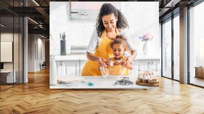 smiling african american mother helping daughter breaking egg for preparing dough in kitchen Wall mural