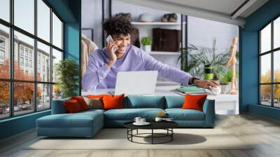 Smiling african american owner of showroom talking on smartphone and holding baseball ball Wall mural