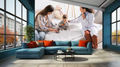 smiling african american pediatrician in white coat sitting on bed and examining baby boy with stethoscope Wall mural