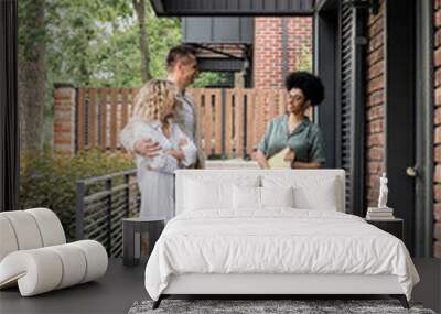 smiling african american real estate agent with folder talking to couple of new owners near house Wall mural