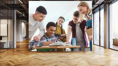 smiling african american schoolboy writing in notebook while his classmates standing around Wall mural