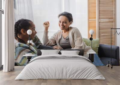 smiling african american woman talking with teenage daughter on couch at home Wall mural