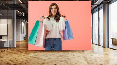 smiling and attractive woman in white sweater holding shopping bags isolated on pink Wall mural