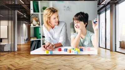 smiling child psychologist and kid with dyslexia playing with building blocks Wall mural