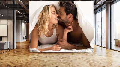 smiling couple going to kiss under sleeping sheets in the morning Wall mural