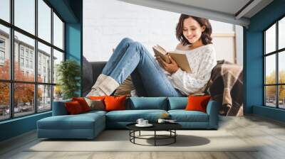 smiling girl reading book on sofa at home Wall mural