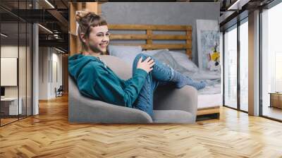 smiling girl sitting on armchair in bedroom and looking away Wall mural