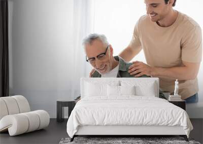 smiling guy touching shoulders of pleased dad opening fathers day present Wall mural