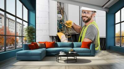 smiling handsome electrician repairing electrical box with pliers in corridor and looking at camera Wall mural