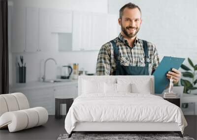 smiling handsome plumber holding clipboard and looking at camera in kitchen Wall mural