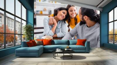 Smiling hispanic girl embracing parents near bowls of cereals on blurred foreground Wall mural