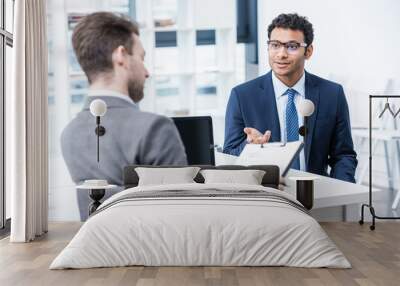 smiling man in suit and eyeglasses gesturing and looking at businessman with clipboard, business con Wall mural