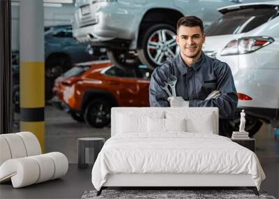 smiling mechanic looking at camera while standing with crossed arms and holding wrenches Wall mural