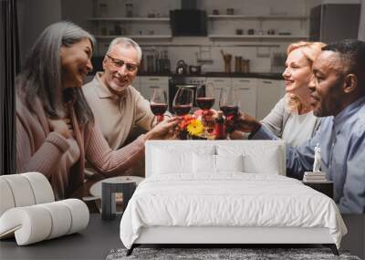 smiling multicultural friends clinking with wine glasses during dinner Wall mural