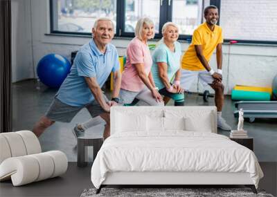 smiling senior multiethnic sportspeople synchronous stretching at sports hall Wall mural