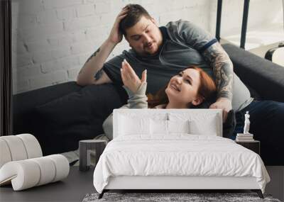 smiling size plus boyfriend and girlfriend talking and lying on sofa at home Wall mural