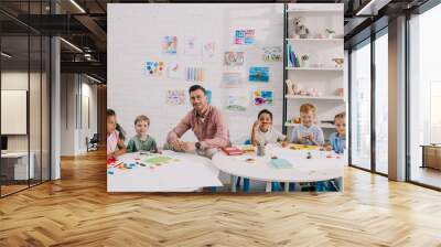 smiling teacher and multiethnic kids sitting at table with colorful plasticine in classroom Wall mural