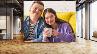 Smiling teen girl holding cup and looking at camera near boyfriend at home, banner. Wall mural