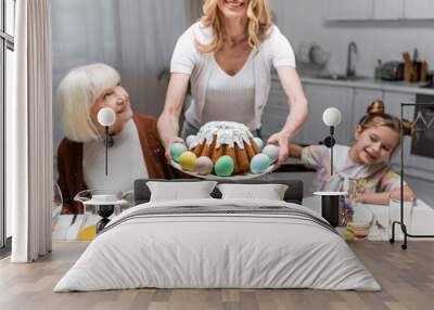 smiling woman holding easter cake with painted eggs near mother and daughter. Wall mural