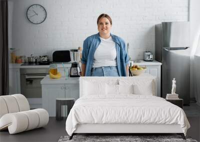 Smiling woman with overweight standing near food in kitchen Wall mural