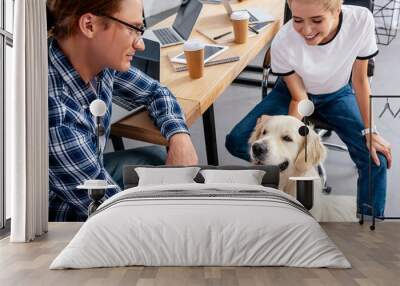 smiling young colleagues looking at dog in office Wall mural